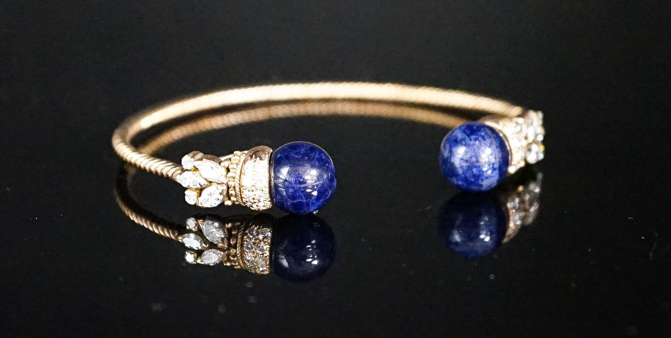 A modern yellow metal twist, two stone sodalite? and diamond set open bangle, gross weight 14 grams.